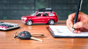 Car loan or buying a new car concept. Car key on table with a man signing on leasing or document form and red car in background. Leasing and insurance business.