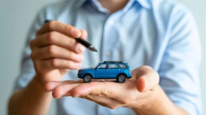 Automobile Financial Planning Hand Holding Miniature Car with Pen Symbolizing Important Decisions